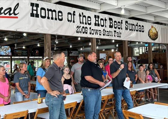Secretary Naig (right), Bryan Whaley (center), and Greene County Cattleman Bill Fields (left) are flanked by cattle farmers from Calhoun, Pocahontas, and Webster Counties at the Cattlemen's Beef Quarters at the 2026 Iowa State Fa